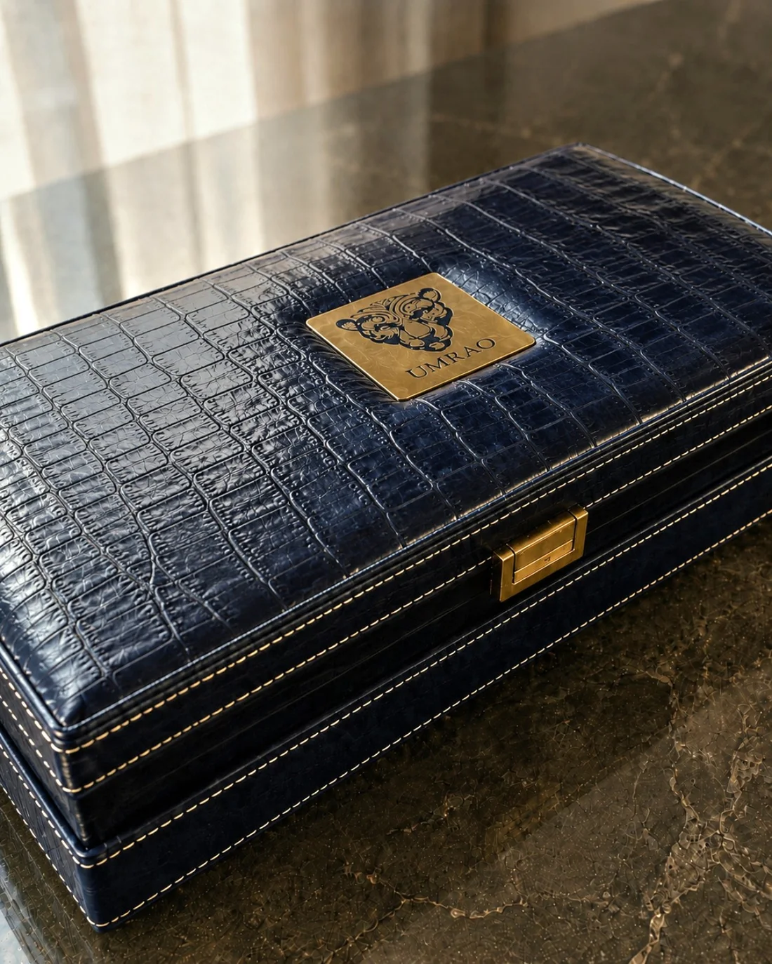A closed navy crocodile-grain coffret with its metal crest